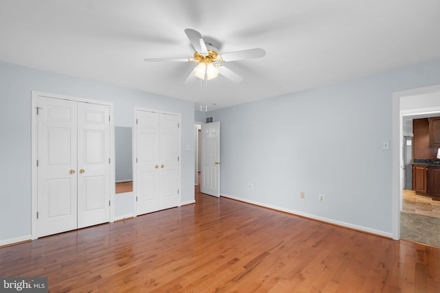 unfurnished bedroom with multiple closets, light wood-style flooring, baseboards, and ceiling fan