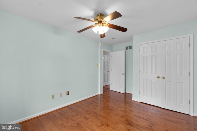 unfurnished bedroom featuring baseboards, wood finished floors, a closet, and a ceiling fan