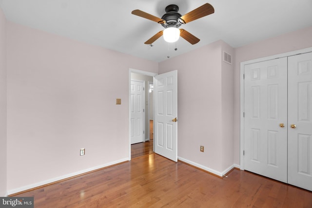 unfurnished bedroom featuring wood finished floors, baseboards, a closet, and ceiling fan