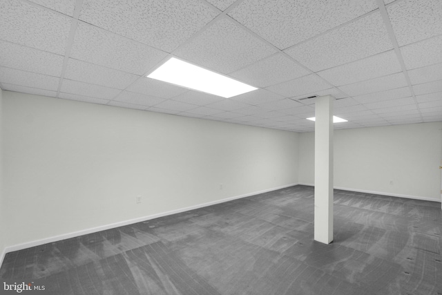 finished basement with dark colored carpet, a paneled ceiling, and baseboards