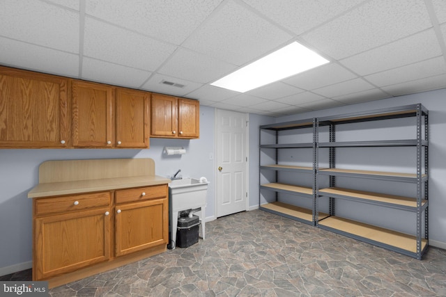 finished below grade area featuring a drop ceiling, baseboards, and stone finish flooring