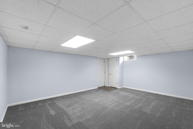 finished below grade area featuring dark carpet, baseboards, and a drop ceiling