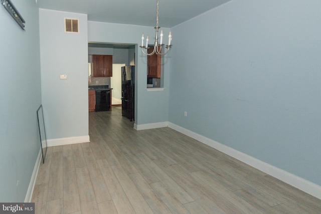 unfurnished room featuring a chandelier, wood finished floors, and baseboards