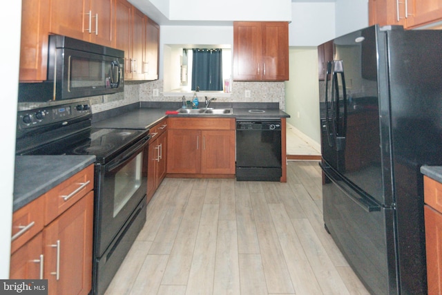 kitchen with black appliances, a sink, light wood finished floors, dark countertops, and decorative backsplash
