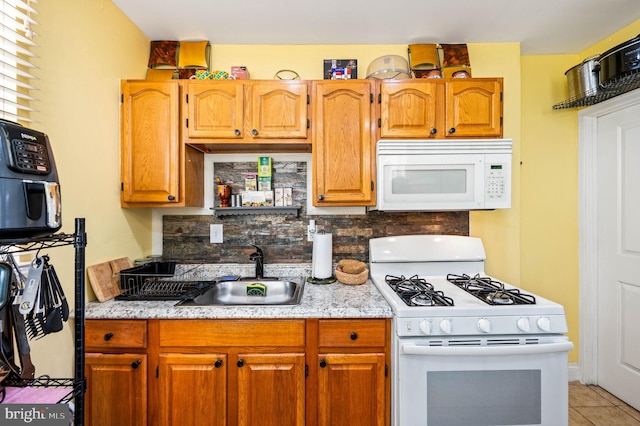 kitchen with white appliances, a sink, tasteful backsplash, light tile patterned flooring, and brown cabinetry