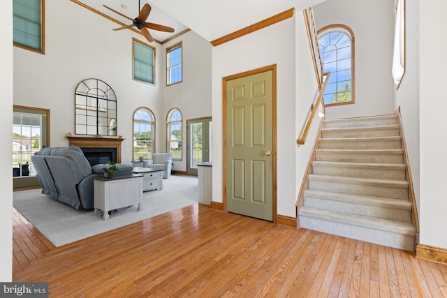 living area featuring a towering ceiling, light wood finished floors, healthy amount of natural light, ceiling fan, and a glass covered fireplace