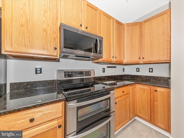 kitchen with appliances with stainless steel finishes, dark stone counters, and light tile patterned flooring