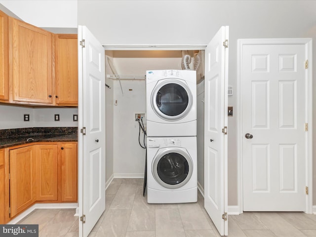 laundry area with stacked washing machine and dryer, light tile patterned floors, and baseboards