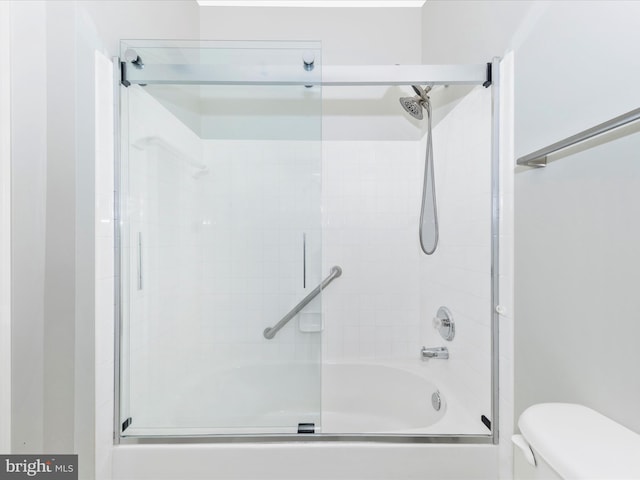 bathroom featuring toilet and bath / shower combo with glass door