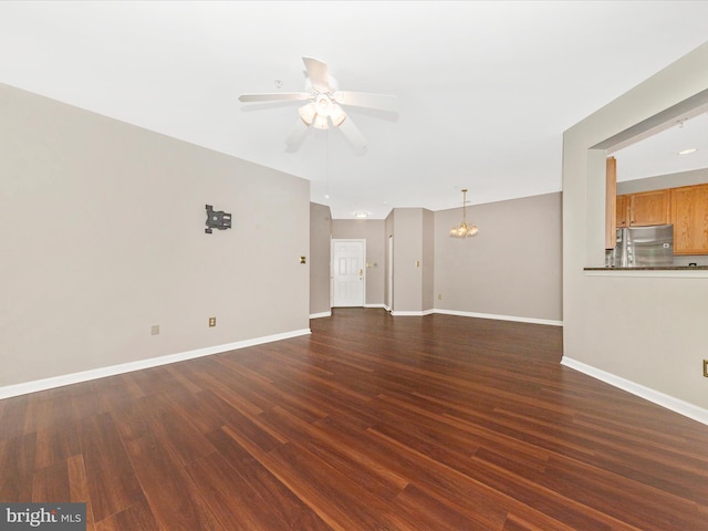 unfurnished living room with ceiling fan, dark wood finished floors, baseboards, and a chandelier