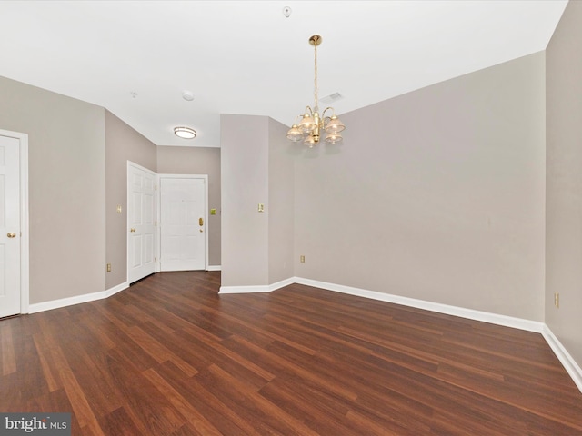 empty room with a chandelier, wood finished floors, and baseboards