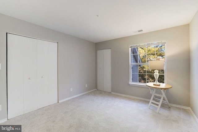 unfurnished bedroom with multiple closets, light carpet, and baseboards