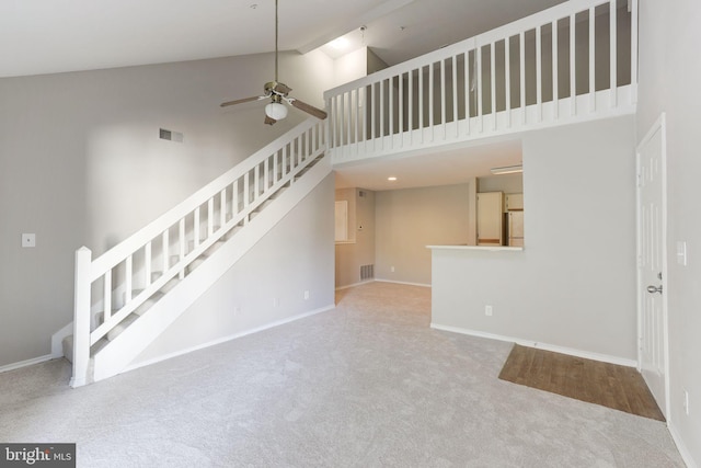 unfurnished living room with high vaulted ceiling, ceiling fan, carpet, stairs, and baseboards