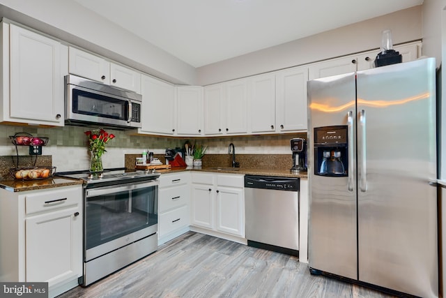 kitchen with stainless steel appliances, dark stone countertops, white cabinets, and backsplash