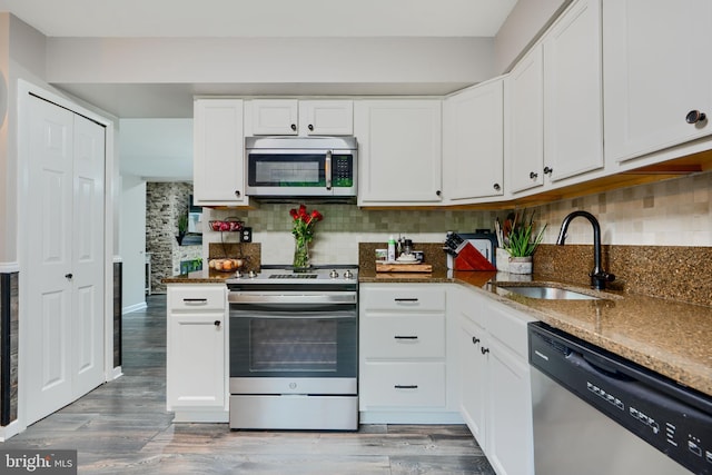 kitchen with stainless steel appliances, a sink, dark stone countertops, backsplash, and white cabinetry