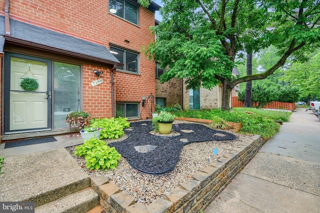 doorway to property featuring brick siding and fence