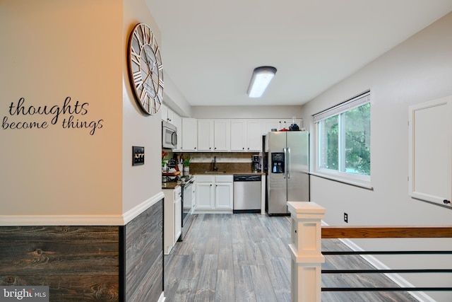 kitchen with appliances with stainless steel finishes, dark countertops, white cabinetry, light wood-style floors, and a sink