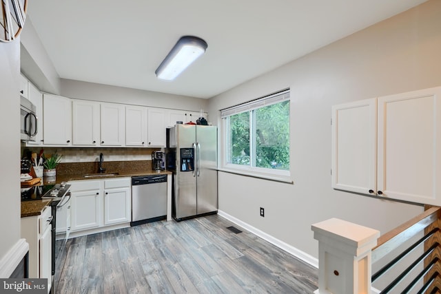 kitchen with appliances with stainless steel finishes, a sink, light wood-style floors, white cabinets, and baseboards