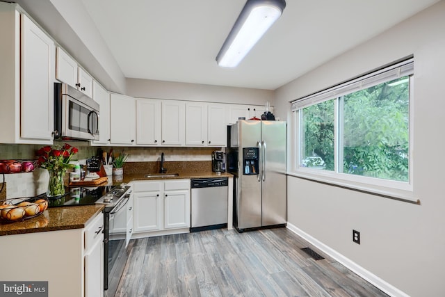 kitchen featuring stainless steel appliances, a sink, light wood finished floors, white cabinets, and decorative backsplash