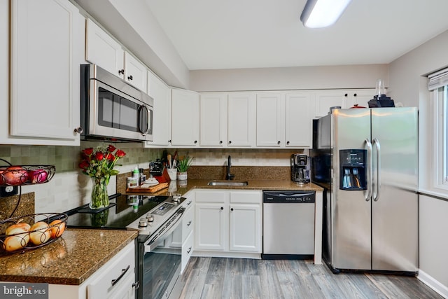 kitchen featuring appliances with stainless steel finishes, a sink, white cabinets, light wood-type flooring, and backsplash