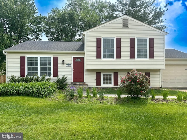 split level home with a front yard, an attached garage, and a shingled roof