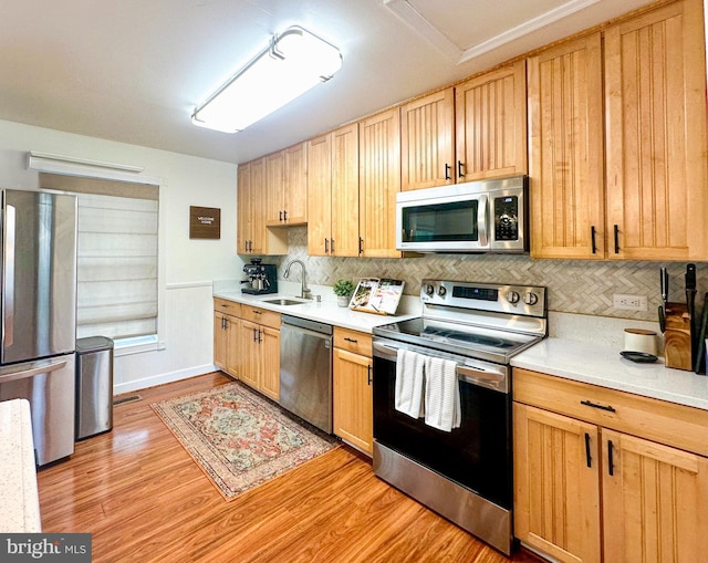 kitchen with stainless steel appliances, a sink, light countertops, and light wood-style flooring