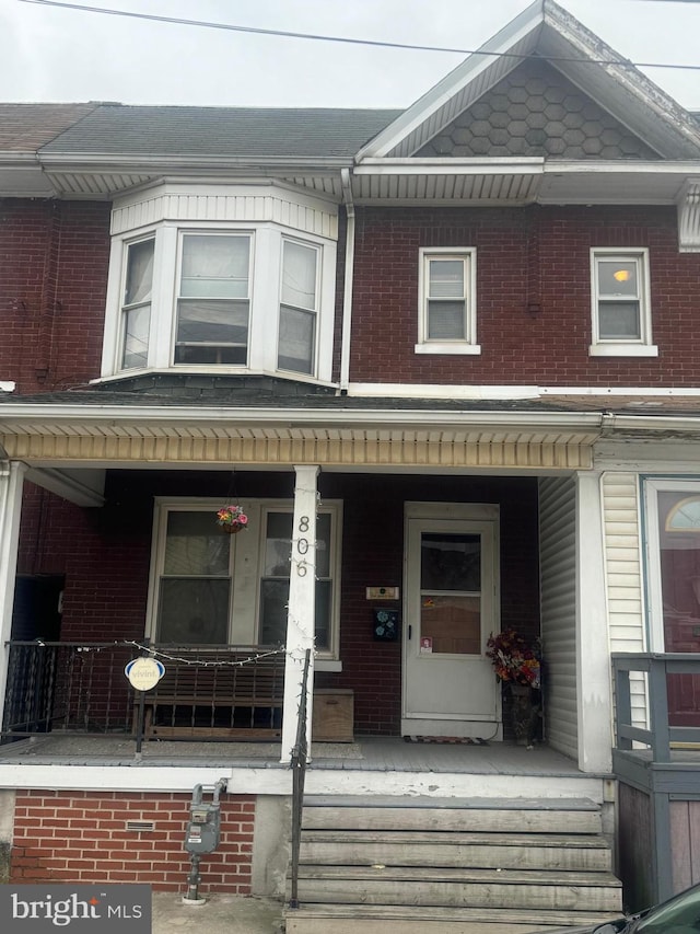 townhome / multi-family property featuring covered porch and brick siding
