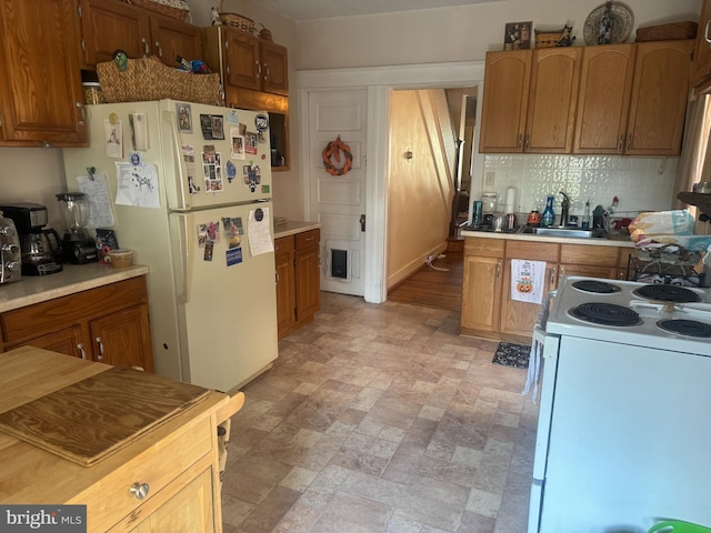 kitchen featuring white appliances, a sink, stone finish floors, backsplash, and brown cabinetry