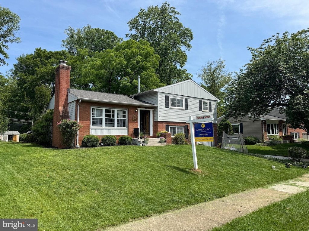 split level home with brick siding, a front lawn, and a chimney