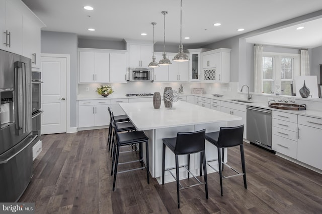 kitchen featuring appliances with stainless steel finishes, a sink, a breakfast bar area, a center island, and dark wood finished floors