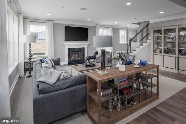 living area featuring ornamental molding, recessed lighting, a glass covered fireplace, stairs, and wood finished floors