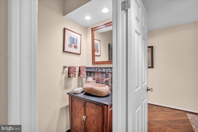 bathroom featuring baseboards, wood finished floors, vanity, and recessed lighting