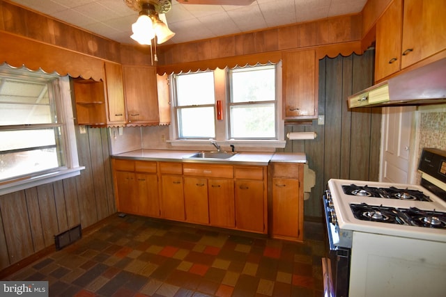 kitchen with gas range gas stove, wooden walls, under cabinet range hood, light countertops, and a sink
