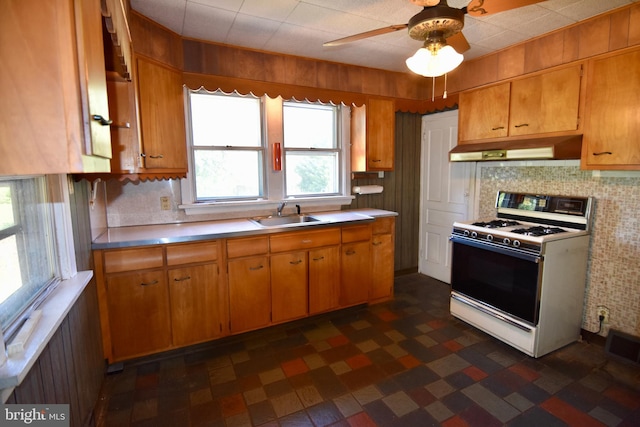 kitchen featuring white range with gas cooktop, under cabinet range hood, a sink, and tasteful backsplash