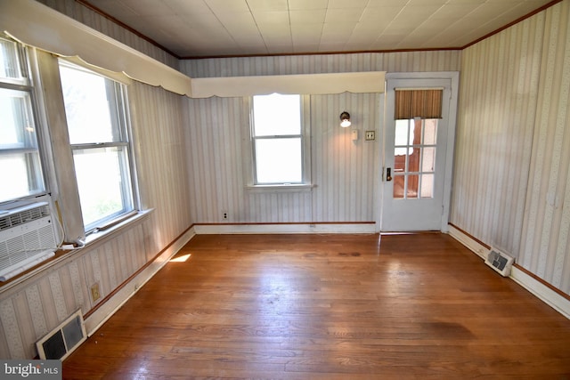 empty room with hardwood / wood-style floors, ornamental molding, baseboards, wallpapered walls, and cooling unit