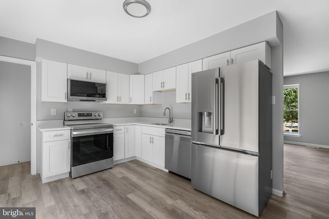 kitchen with stainless steel appliances, a sink, light countertops, white cabinetry, and light wood-style floors