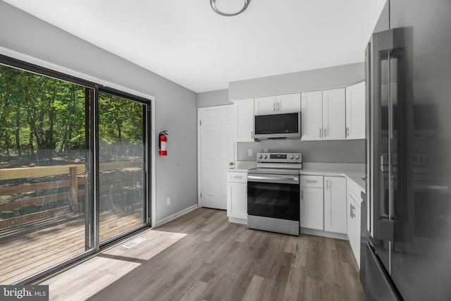 kitchen with stainless steel appliances, light countertops, white cabinets, light wood finished floors, and baseboards