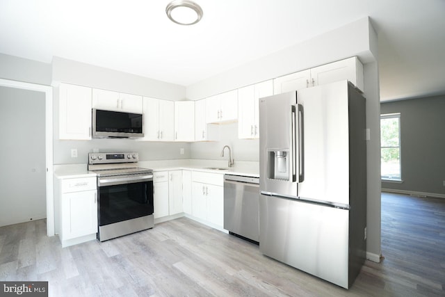 kitchen featuring appliances with stainless steel finishes, a sink, light countertops, light wood-style floors, and white cabinetry