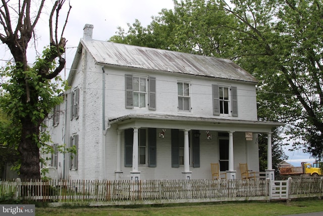 view of front of property featuring covered porch, a chimney, a fenced front yard, and brick siding