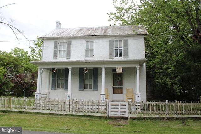 view of front facade featuring a porch, brick siding, a fenced front yard, a chimney, and metal roof