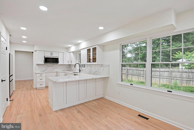 2144 Silentree Dr, Vienna, VA 22182 - kitchen featuring stainless steel microwave, a peninsula, decorative backsplash, white cabinets, and glass insert cabinets