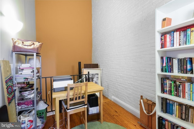 office area featuring brick wall, wood finished floors, and baseboards