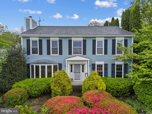 colonial home with a chimney and roof with shingles