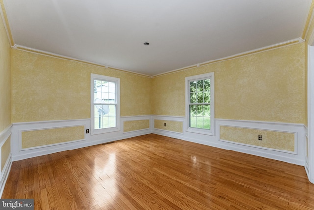 spare room featuring ornamental molding, healthy amount of natural light, wood-type flooring, and a wainscoted wall