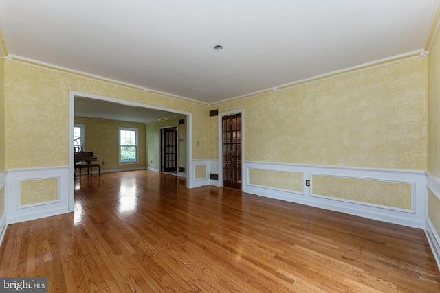 unfurnished room featuring ornamental molding, wood finished floors, and a wainscoted wall