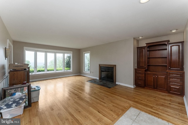unfurnished living room with light wood-style floors, baseboards, a fireplace with flush hearth, and recessed lighting