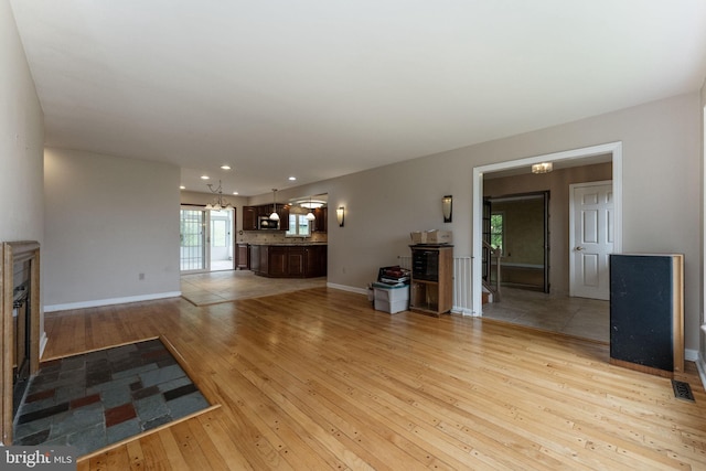 unfurnished living room with light wood-style floors, recessed lighting, baseboards, and a chandelier