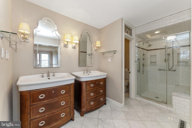 bathroom featuring a shower stall, two vanities, baseboards, and toilet