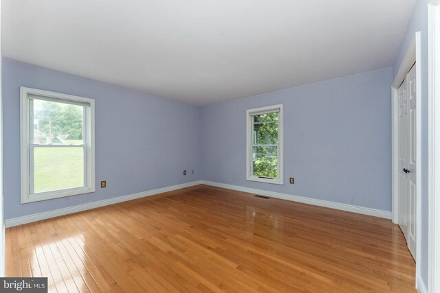 unfurnished bedroom featuring multiple windows, light wood finished floors, and baseboards