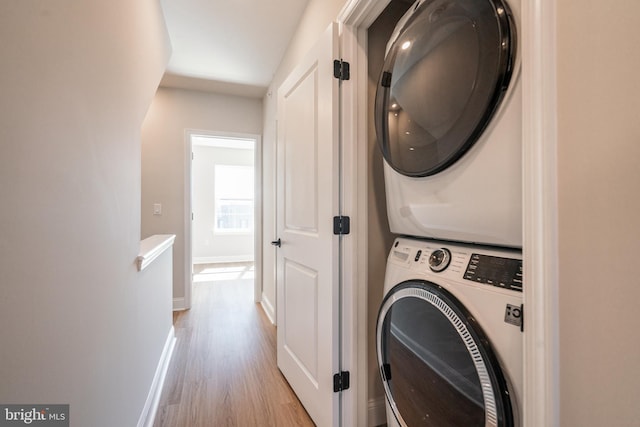 clothes washing area with stacked washer / drying machine, wood finished floors, and baseboards